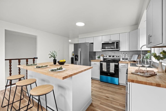 kitchen with appliances with stainless steel finishes, butcher block countertops, a kitchen bar, light wood-style floors, and decorative backsplash