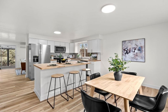 kitchen featuring appliances with stainless steel finishes, a kitchen island, decorative backsplash, white cabinetry, and a breakfast bar