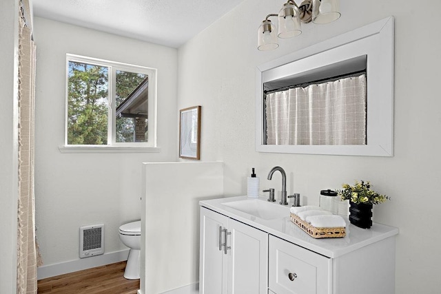 bathroom with toilet, baseboards, wood finished floors, vanity, and heating unit
