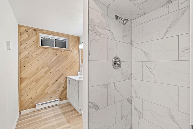 bathroom featuring a baseboard heating unit, wooden walls, tiled shower, wood finished floors, and baseboards
