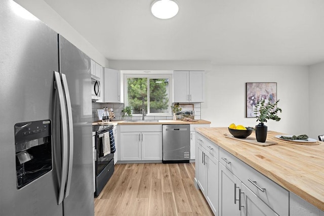 kitchen featuring stainless steel appliances, butcher block countertops, light wood-style flooring, decorative backsplash, and white cabinets