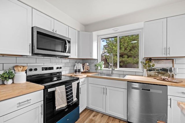 kitchen with appliances with stainless steel finishes, a sink, butcher block counters, white cabinets, and backsplash