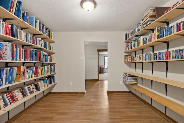living area with wood finished floors, baseboards, a textured ceiling, and wall of books