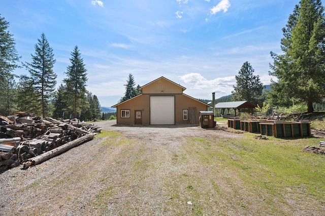 rear view of property featuring an outdoor structure, a detached garage, driveway, and an outbuilding