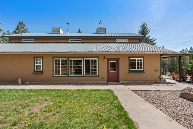 rear view of property with a chimney, metal roof, and a yard