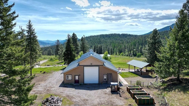 detached garage featuring a vegetable garden, a view of trees, a mountain view, and dirt driveway