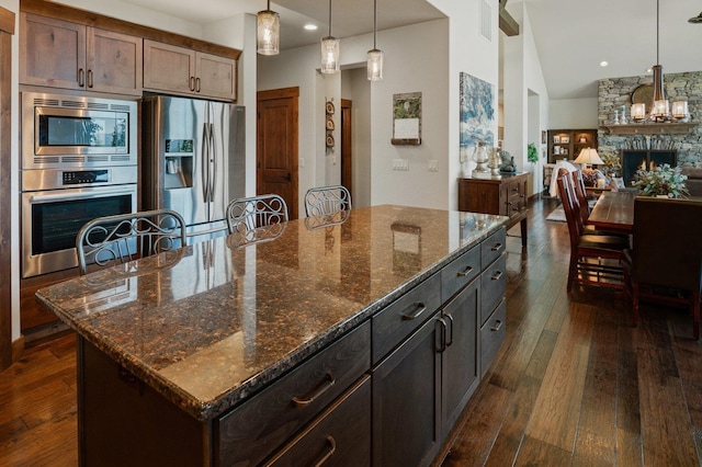 kitchen with stainless steel appliances, dark wood-style flooring, decorative light fixtures, a large island, and dark stone counters