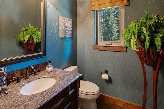 half bath featuring toilet, wallpapered walls, and vanity