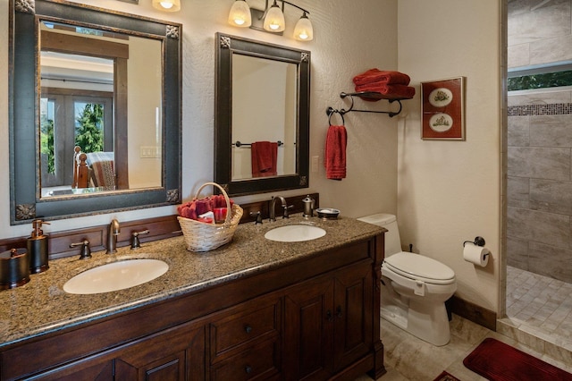 bathroom featuring toilet, tiled shower, and double vanity