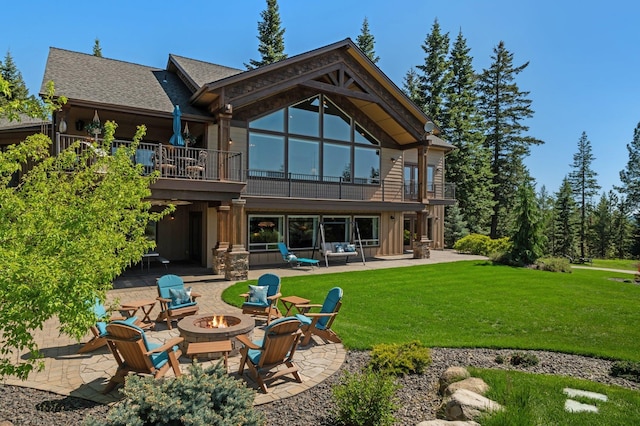 rear view of house with a balcony, a fire pit, a patio, and a lawn
