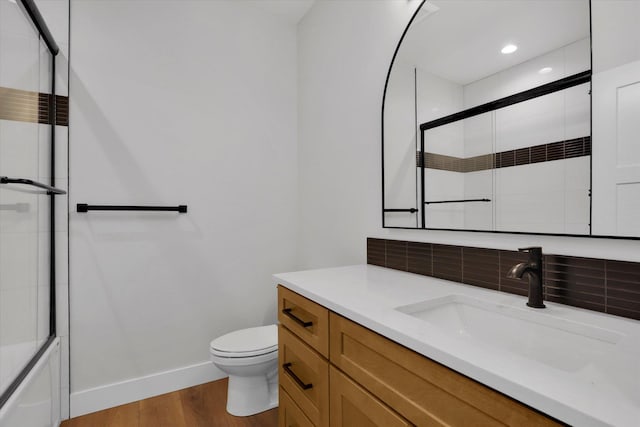 7025 E Beverly Ave, Spokane Valley, WA 99212 - bathroom with wood finished floors, baseboards, toilet, vanity, and decorative backsplash