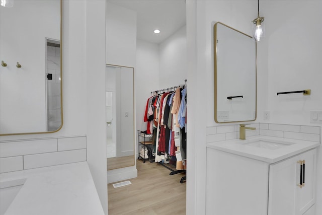bathroom featuring wood finished floors, tasteful backsplash, vanity, a spacious closet, and recessed lighting