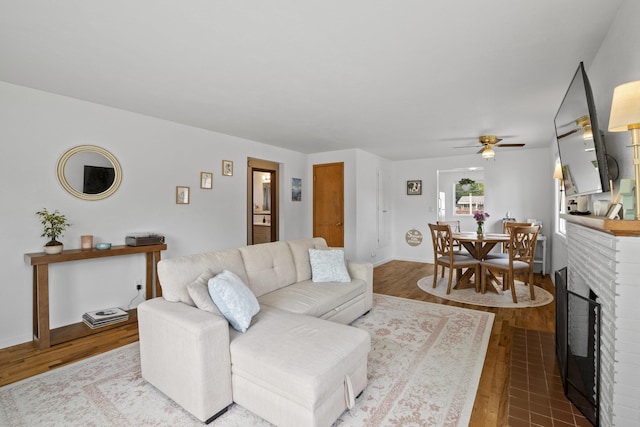 living room featuring ceiling fan, wood finished floors, a brick fireplace, and baseboards