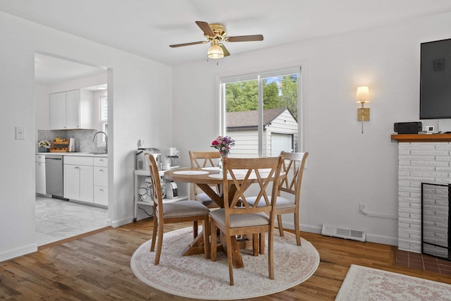 dining room featuring a ceiling fan, light wood-type flooring, a fireplace, and baseboards