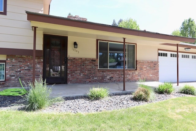 13703 E 31st Ave, Spokane Valley, WA 99216 - doorway to property featuring brick siding, an attached garage, and covered porch