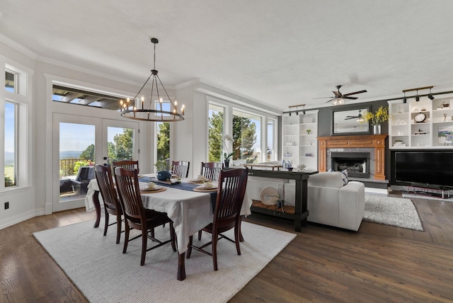 dining area featuring a chandelier, crown molding, dark wood finished floors, a fireplace with raised hearth, and ceiling fan