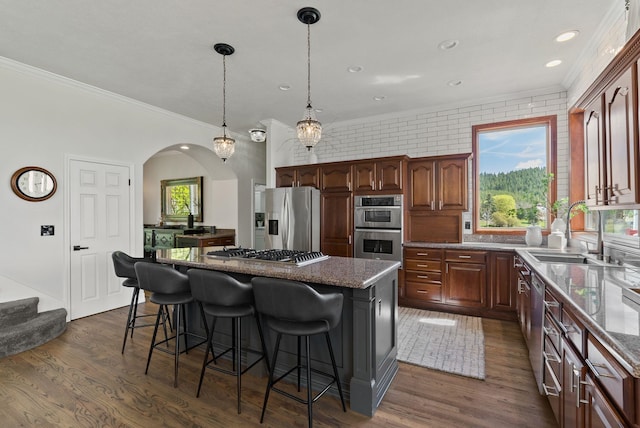 kitchen with stainless steel appliances, a sink, crown molding, a kitchen island, and a breakfast bar area