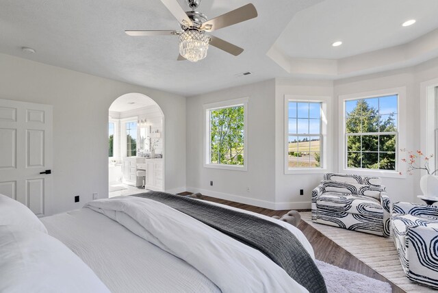 bedroom with baseboards, arched walkways, wood finished floors, a ceiling fan, and ensuite bath
