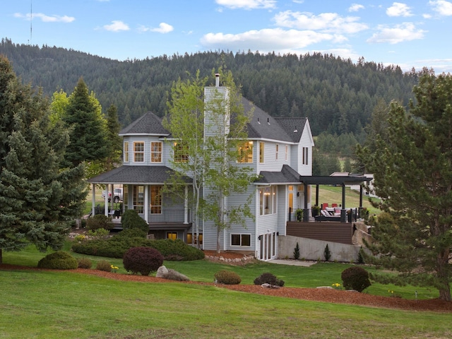 view of front facade featuring a view of trees, a front lawn, and a chimney