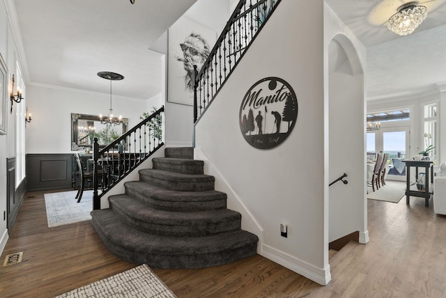 stairway with a chandelier, wood finished floors, crown molding, and baseboards
