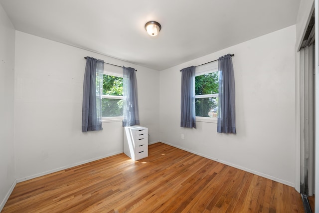 empty room with healthy amount of natural light, light wood-style floors, and baseboards