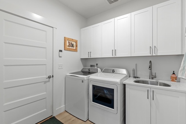 clothes washing area with cabinet space, washer and clothes dryer, and light wood-style flooring