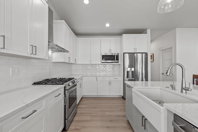 kitchen with stainless steel appliances, a sink, wall chimney exhaust hood, recessed lighting, and light wood-style floors