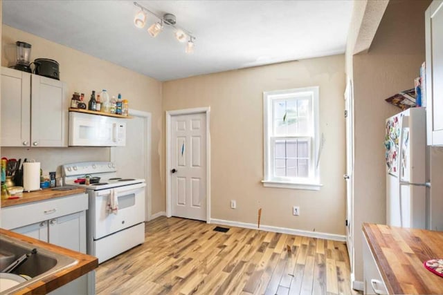 kitchen with white appliances, wood counters, light wood finished floors, and a sink