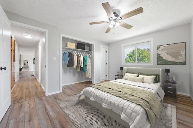 bedroom with a closet, a textured ceiling, wood finished floors, ceiling fan, and baseboards