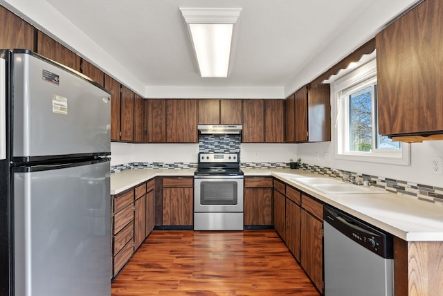 2612 E Longfellow Ave, Spokane, WA 99207 - kitchen featuring appliances with stainless steel finishes, a sink, under cabinet range hood, decorative backsplash, and dark wood-type flooring