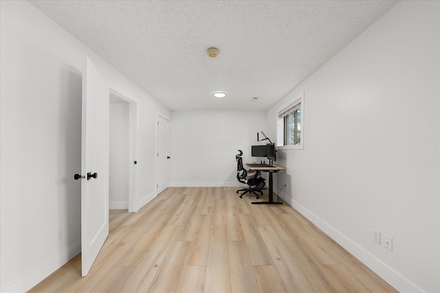 unfurnished office featuring a textured ceiling, light wood-style floors, and baseboards