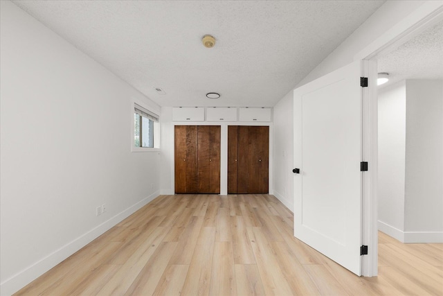 unfurnished bedroom featuring light wood-style floors, a textured ceiling, multiple closets, and baseboards