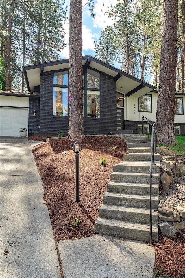 mid-century modern home featuring brick siding, an attached garage, driveway, a porch, and stairway