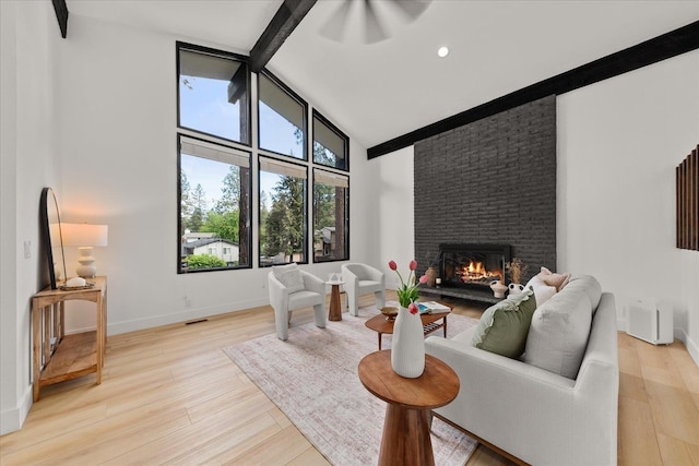 living area with high vaulted ceiling, a brick fireplace, light wood-type flooring, baseboards, and beam ceiling