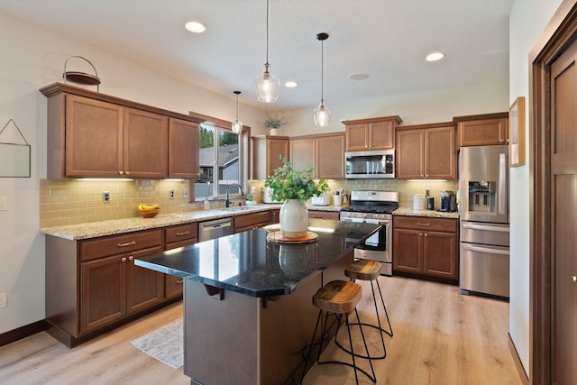 kitchen with stainless steel appliances, a sink, light wood-style floors, backsplash, and a breakfast bar area