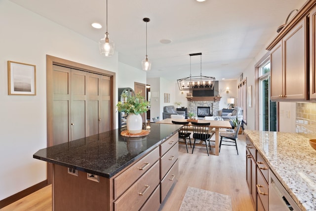 kitchen with a stone fireplace, light wood-style flooring, decorative backsplash, decorative light fixtures, and a kitchen island