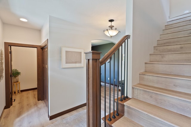 stairway with wood finished floors, arched walkways, and baseboards