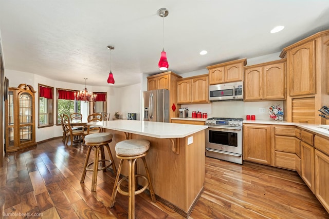 kitchen featuring stainless steel appliances, a center island, a kitchen bar, dark wood-type flooring, and light countertops