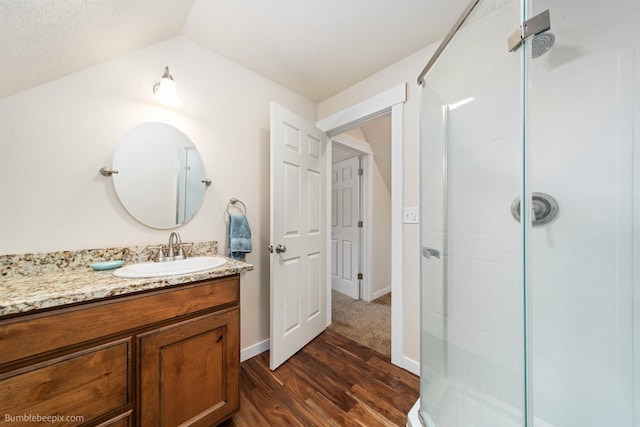 full bath featuring a shower stall, wood finished floors, lofted ceiling, vanity, and baseboards