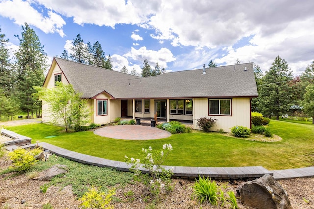 back of house with a shingled roof, a patio area, and a lawn