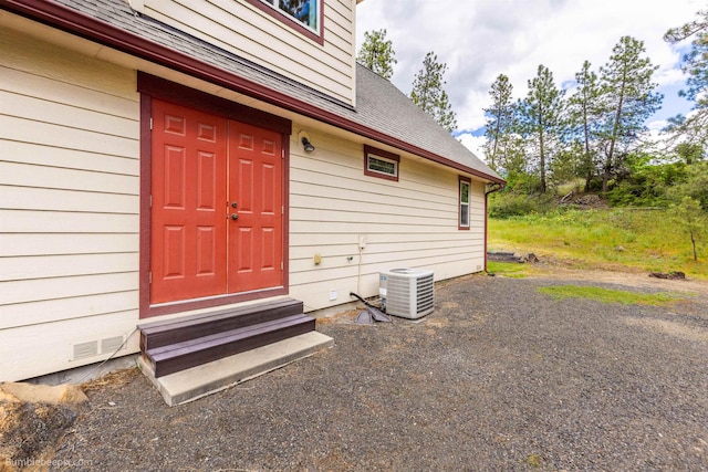 doorway to property with central AC unit and a shingled roof