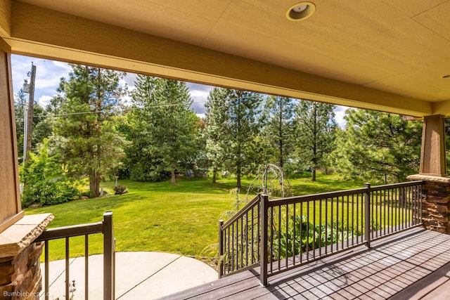 wooden deck with view of scattered trees, a lawn, and a patio