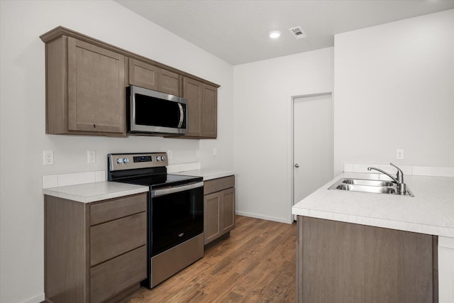 kitchen featuring appliances with stainless steel finishes, a sink, wood finished floors, light countertops, and recessed lighting