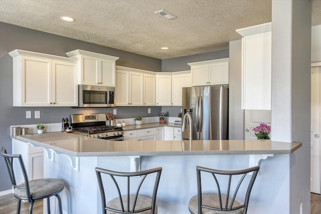 14621 E Sanson Ave, Spokane Valley, WA 99216 - kitchen with stainless steel appliances, a textured ceiling, wood finished floors, a breakfast bar area, and white cabinets