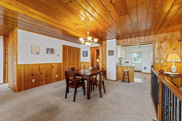 dining area with a chandelier, wood walls, wooden ceiling, light colored carpet, and a wainscoted wall
