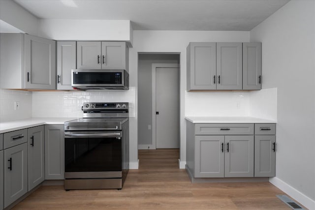 11707 E Broadway Ave, Spokane, WA 99206 - kitchen with stainless steel appliances, gray cabinets, light wood-type flooring, tasteful backsplash, and light countertops