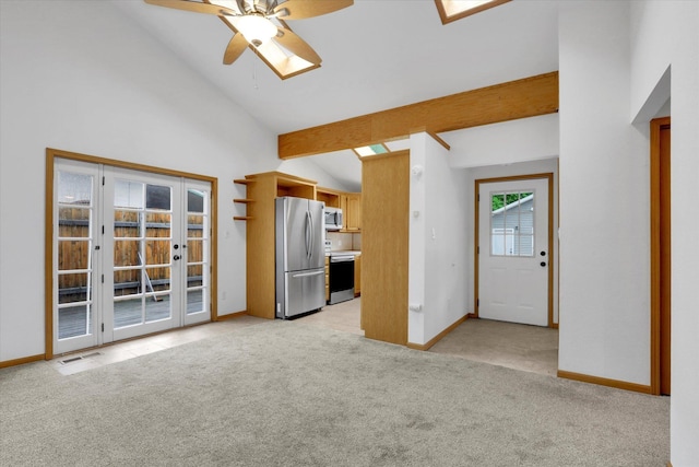 unfurnished living room featuring vaulted ceiling, a ceiling fan, light colored carpet, baseboards, and a skylight