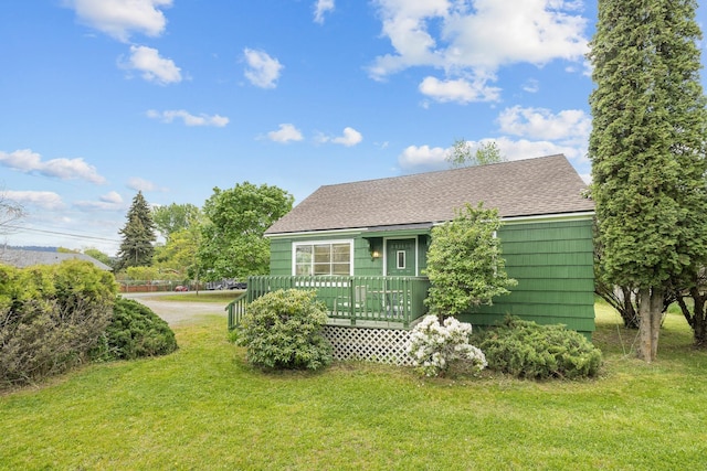 view of side of property featuring a lawn, a shingled roof, and a wooden deck