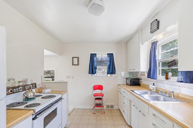 kitchen with electric range, a sink, light countertops, white cabinetry, and baseboards