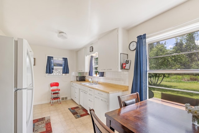 kitchen featuring freestanding refrigerator, a sink, light flooring, light countertops, and white cabinets